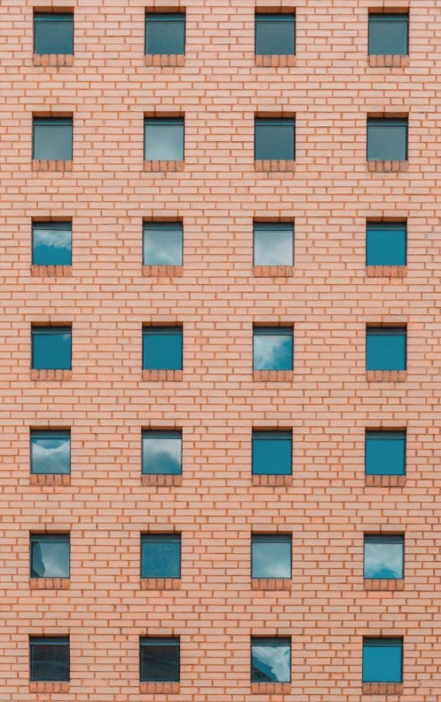 Symmetrical brick facade with evenly spaced square windows reflecting blue sky.